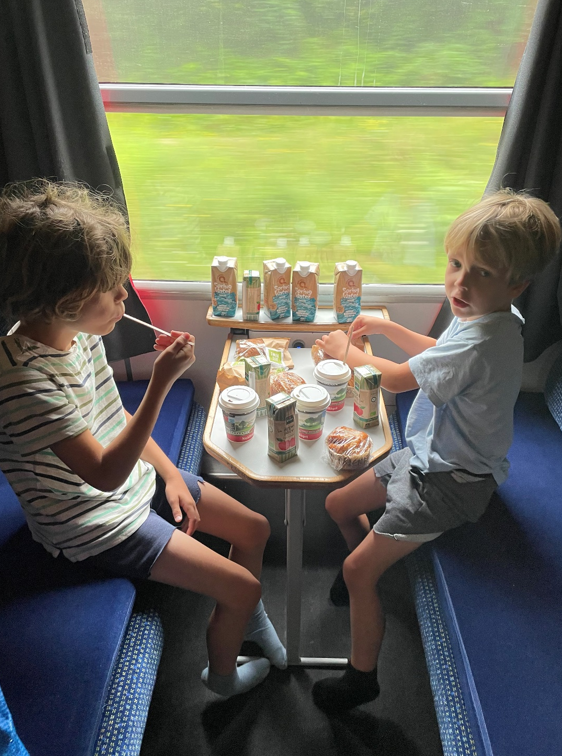 To drenge spiser morgenmad på hver side af lille bord i sovekupe i nattog