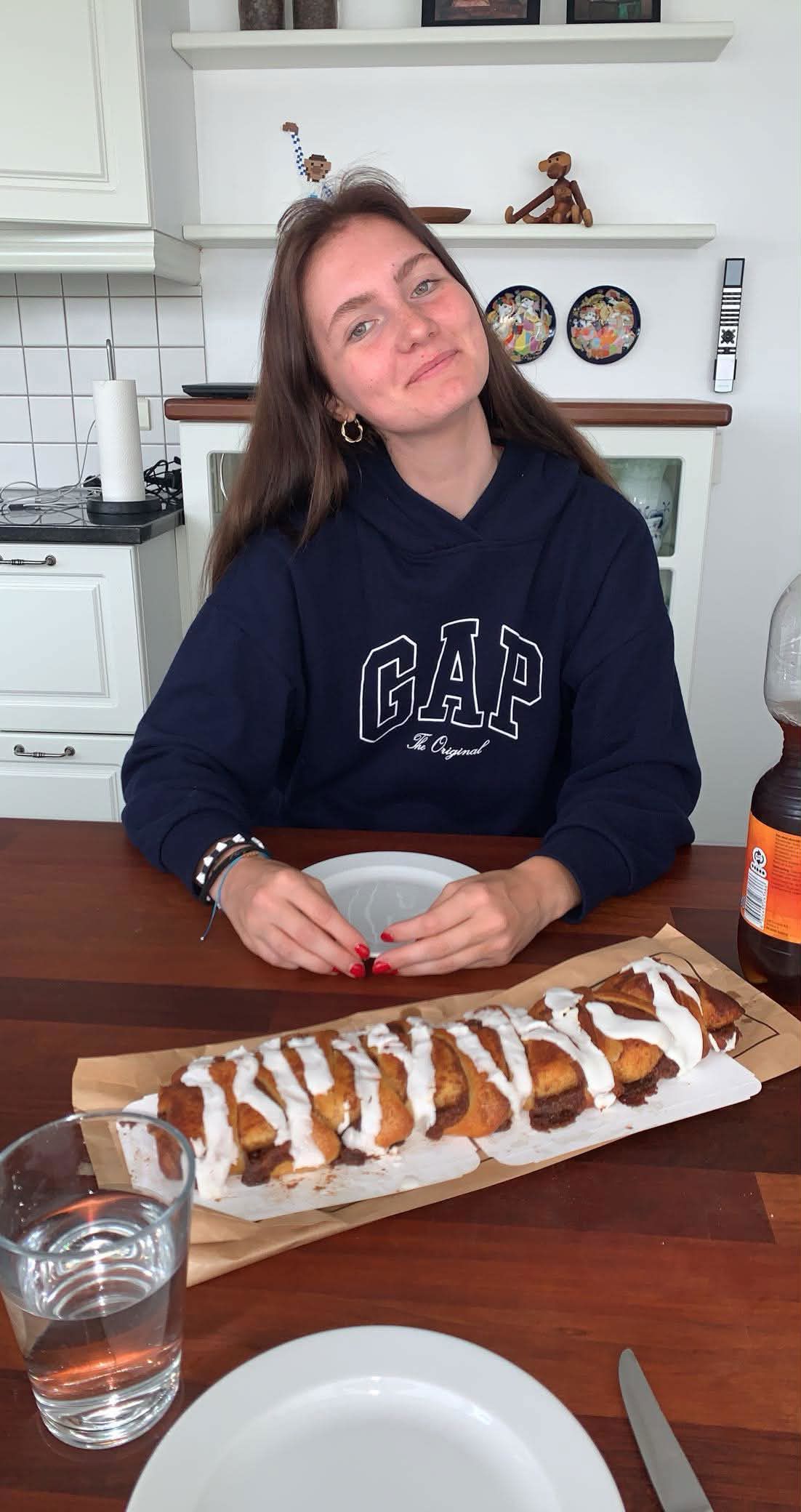 Ung kvinde sidder ved bord, hovedet lidt på skrå og smiler til fotograf