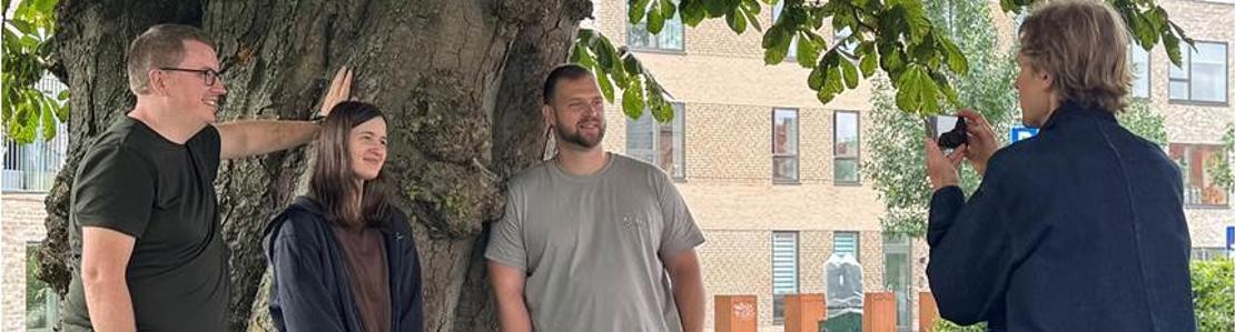 3 personer poserer foran et træ mens en fotograf tager et billede af dem