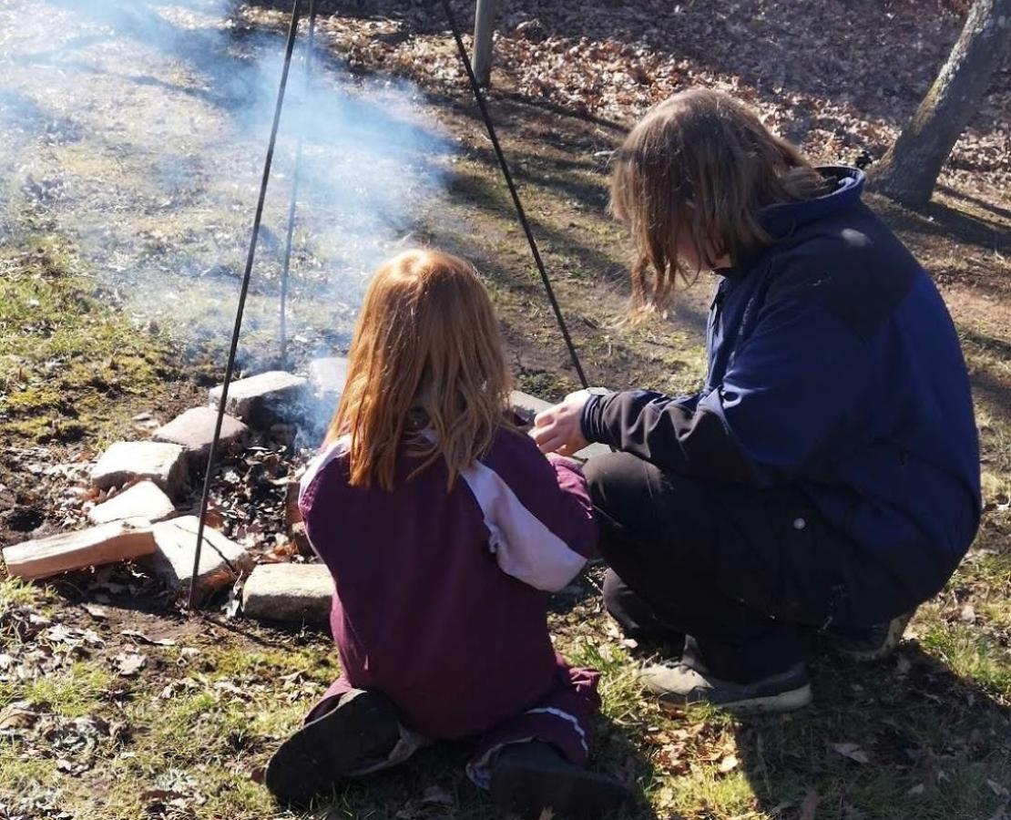 Camilla og datter sidder ved bålsted med ryggen mod fotograf og ansigt mod bålet