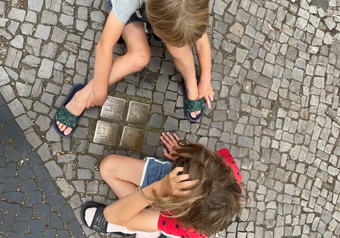 To drenge sidder ved et par af de mange mindesten foran beboelsesejendomme, som viser navne på tidligere beboere, før de blev deporteret nazisterne i berlin