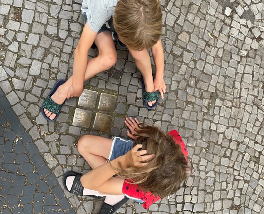 To drenge sidder ved et par af de mange mindesten foran beboelsesejendomme, som viser navne på tidligere beboere, før de blev deporteret nazisterne i berlin