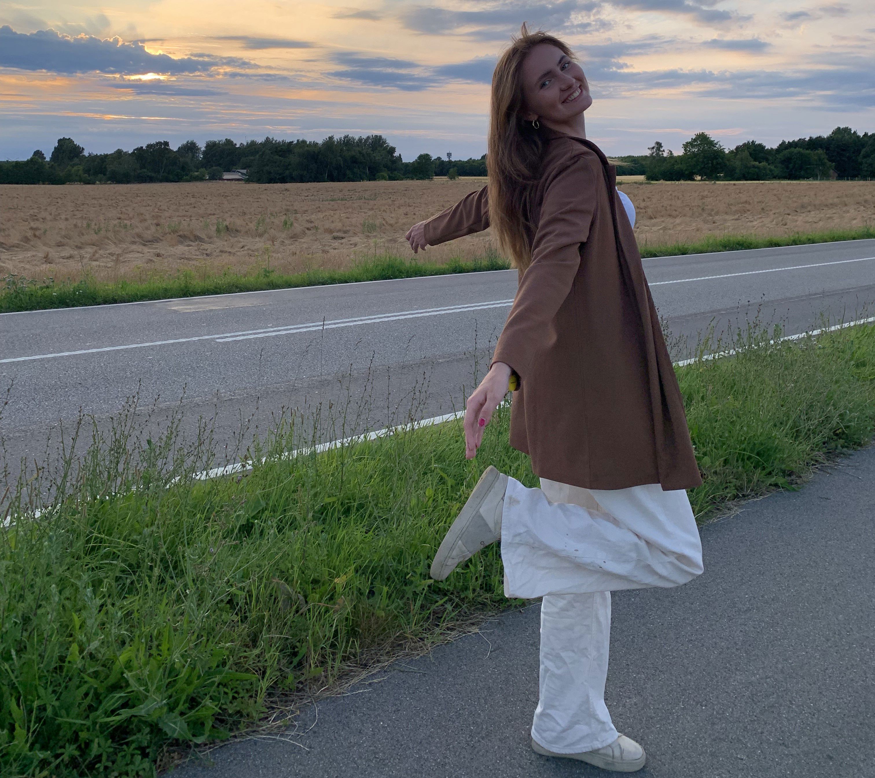 Ung kvinde står på et ben med armene ud til siden og kigger smilende bagud på fotografen