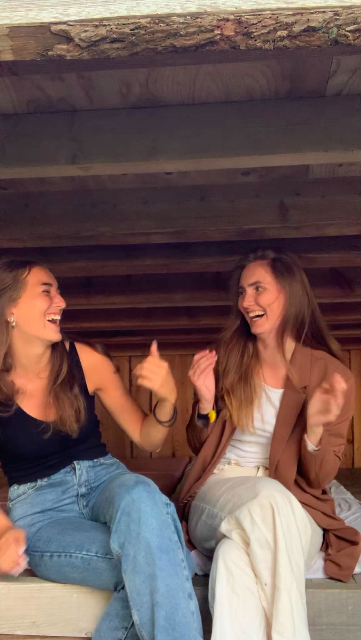 To unge kvinder sidder grinende i et shelter