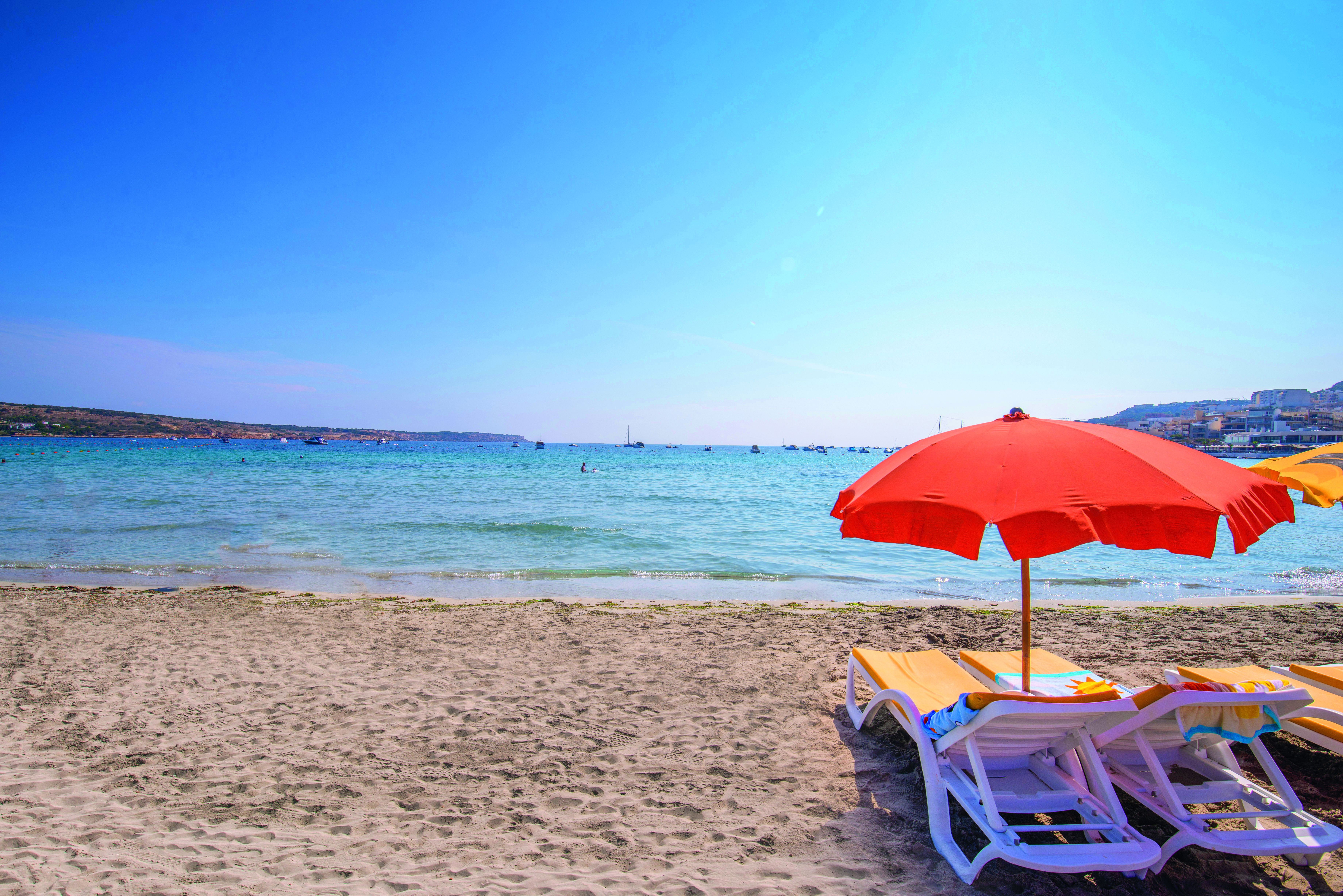 Strand ved Mellieha Holiday Centre: blåt hav, sandstrand og strandsenge med parasol