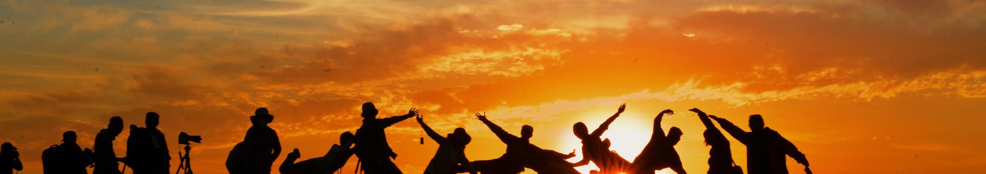 En lang række af mennesker i silhuet mod aftensolen